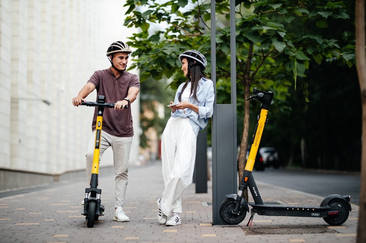 Кикшеринг Whoosh. Молодая пара в велосипедных шлемах на электросамокатах