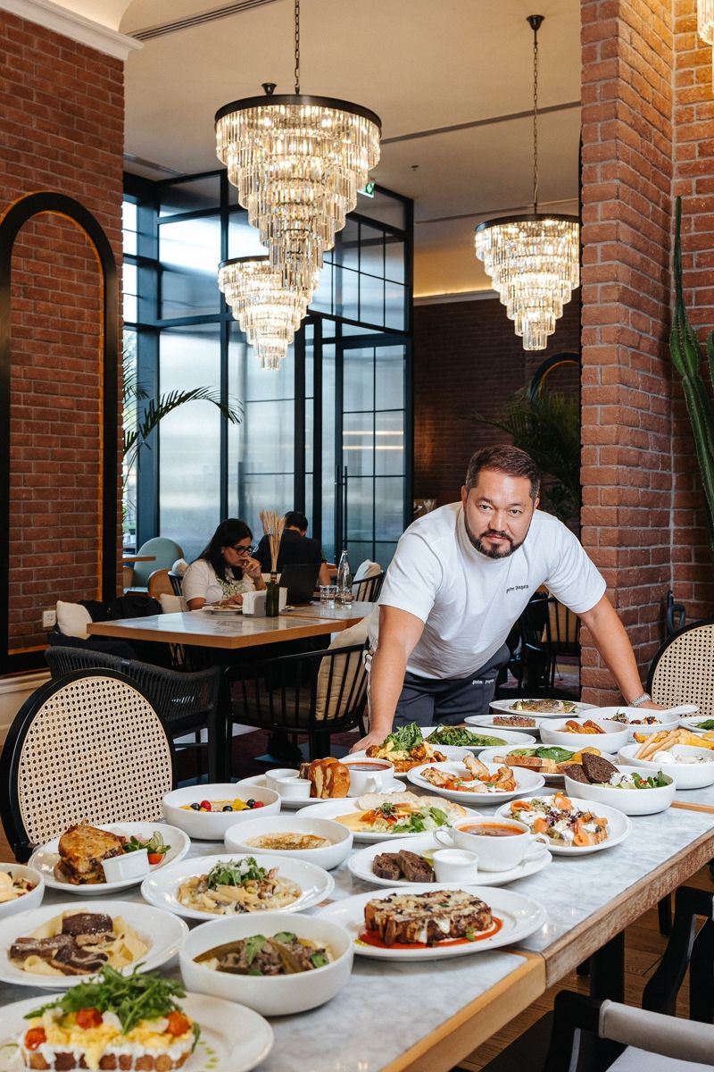 Нурлан Мукушев - ресторатор перед накрытым столом с разными блюдами