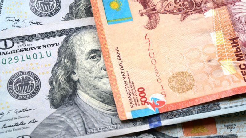 Тенге купюры лежат на купюрах долларов США с портретом Франклина