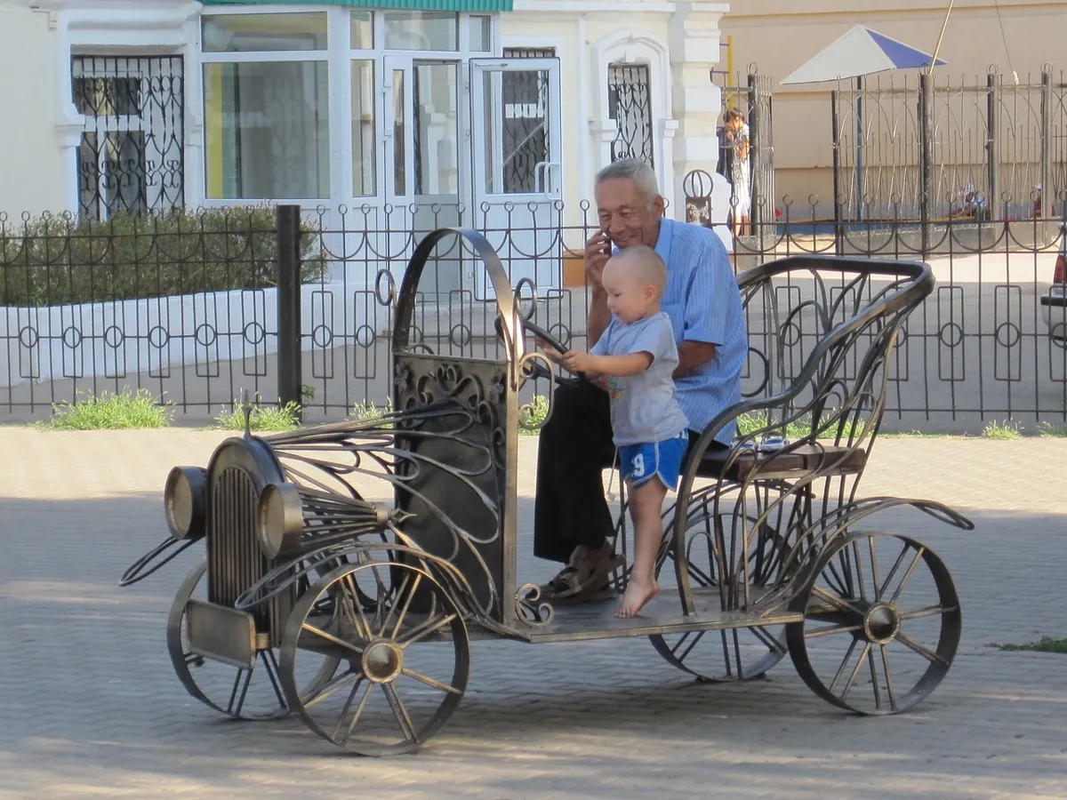 Население Казахстана «стареет» Пожилой мужчина сидит в декоративном автомобиле из металла с маленьким мальчиком