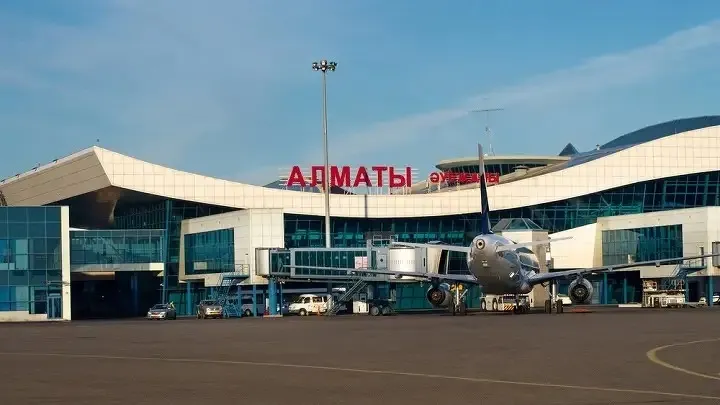 Международный аэропорт Алматы, терминал Т1, здание аэропорта летом, на фоне голубого неба, с трапами для посадки в самолеты
