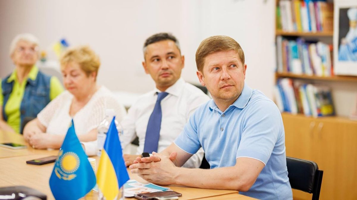 Сергей Нагорняк на мероприятии На переднем плане флаги Казахстан и Украины, двое мужчин, один - Сергей Нагорняк, и женщина сидят за столом на мероприятии в Киеве