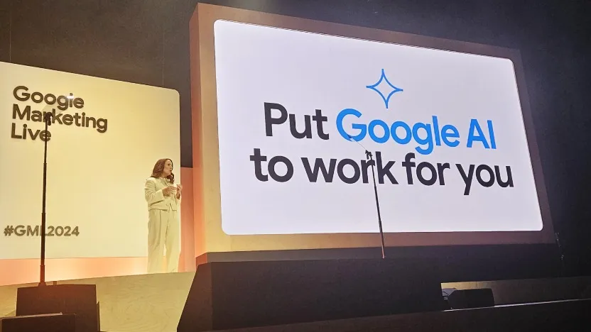 Девушка в белом костюме стоит между двух экранов, на которых написано Google Marketing Live и Put Google AI AI work for you