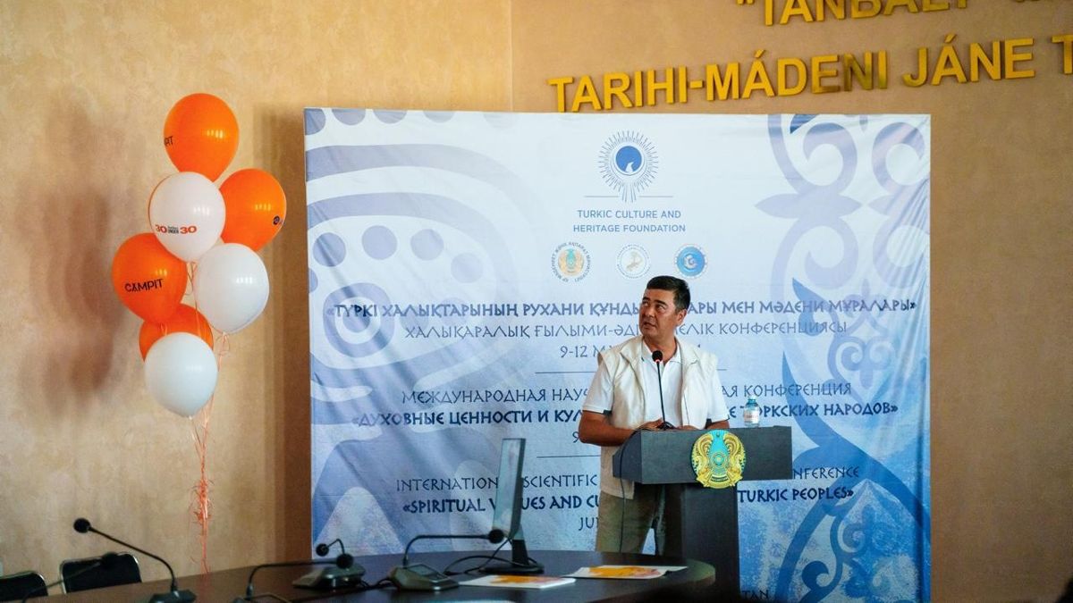 Арманжан Байтасов на фоне презентации о петроглифах