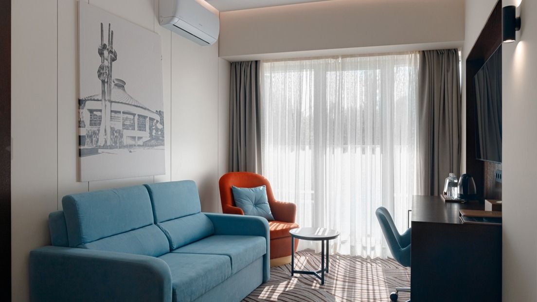 Номер в гостинице, голубой диван, оранжевое кресло, белые занавески, письменный стол