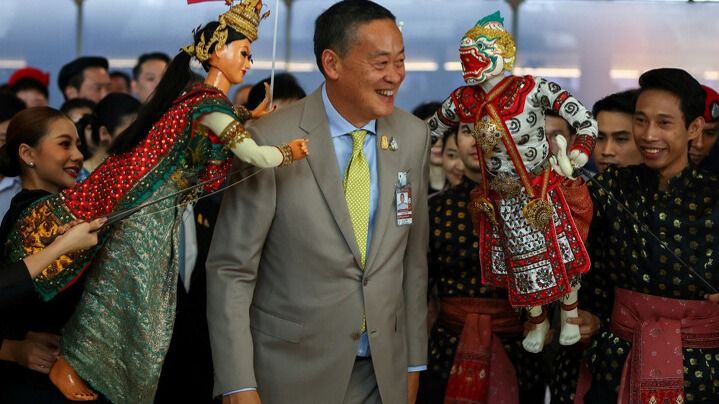Премьер Таиланда Сретта Тависин встречает туристов, мужчина, по сторонам - две традиционные куклы