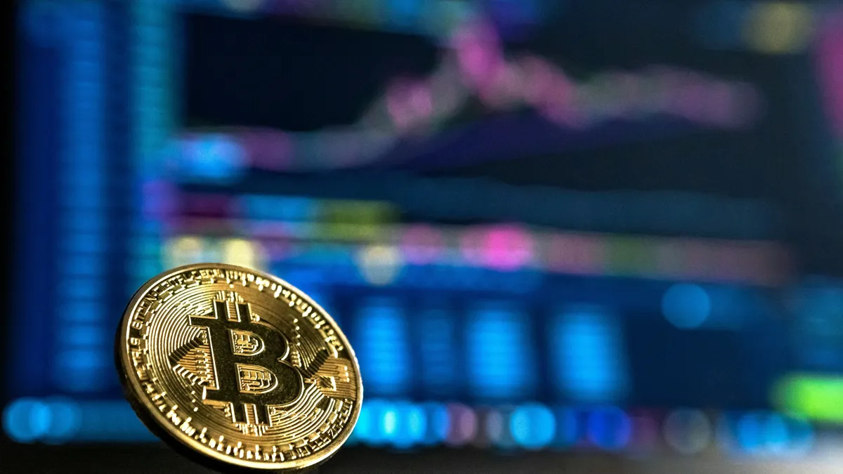 Биткоин в руках на фоне монитора с трендами на рынке крипотовалюты