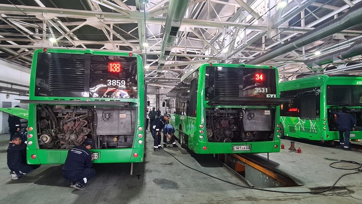 Три зеленых автобуса ремонтируют технические работники в темно-синей униформе