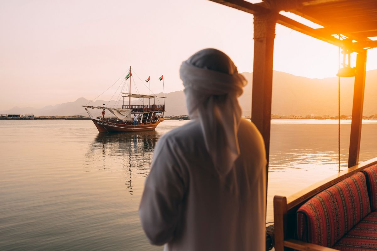 Мужчина в арабской одежде и головном уборе смотрит на лодку в море