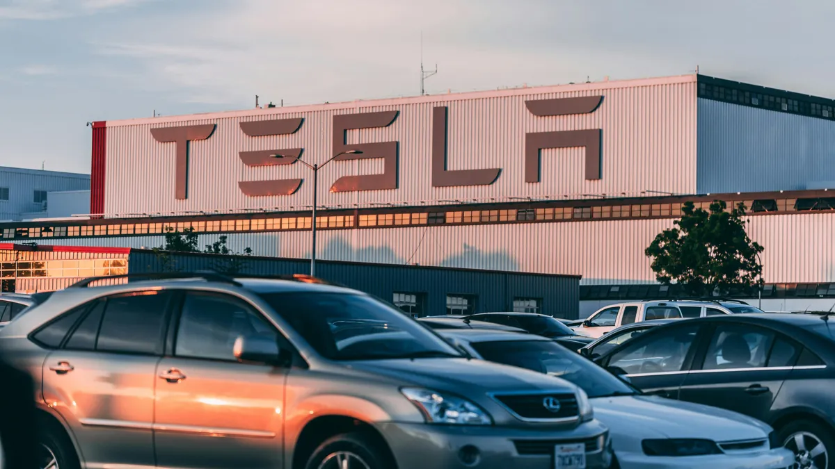 Логотип Tesla на здании, на переднем фоне — автомобили