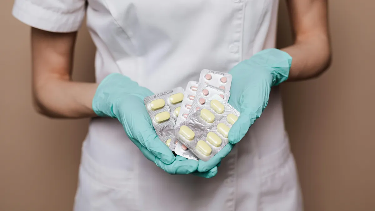 Девушка в белой медицинской форме и в перчатках держит в руках несколько упаковок лекарств