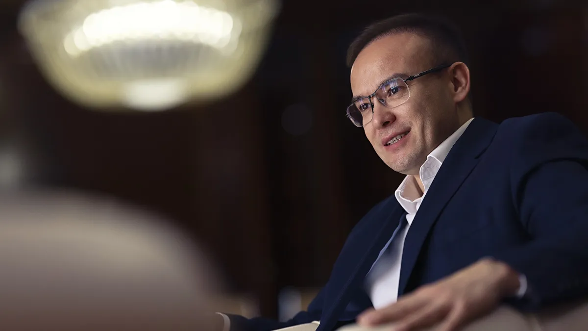 Бекжан Пиртматов, мужчина в пиджаке и белой рубашке сидит, опираясь рукой на спинку кресла 