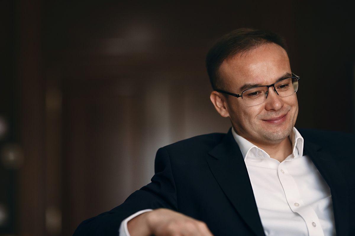Бекжан Пирматов в белой рубашке и темном пиджаке, сидит, в очках