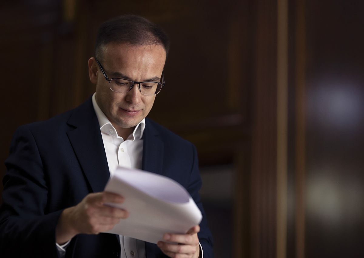 Бекжан Пирматов стоит с листами бумаги в руках, читает документы, в очках