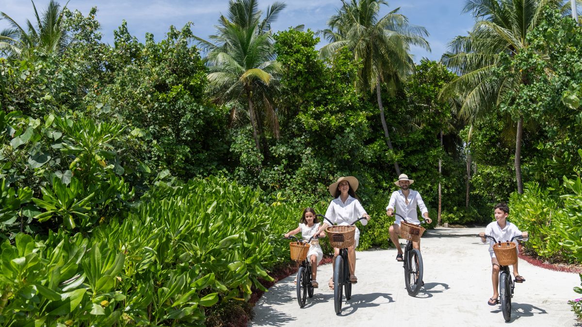 Семья на велосипедах едет по острову на Мальдивах на фоне зелени