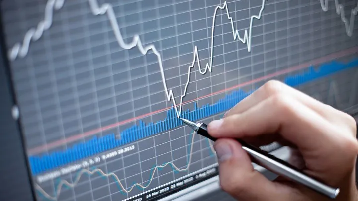 график на дисплее, рука кончиком ручки указывает на нижнюю точку, котировки акций, падение курса акций