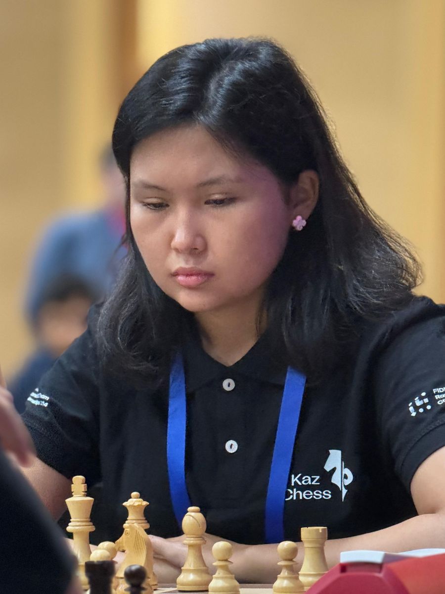 Бибисара Асаубаева, в темной футболке поло, играет в шахматы