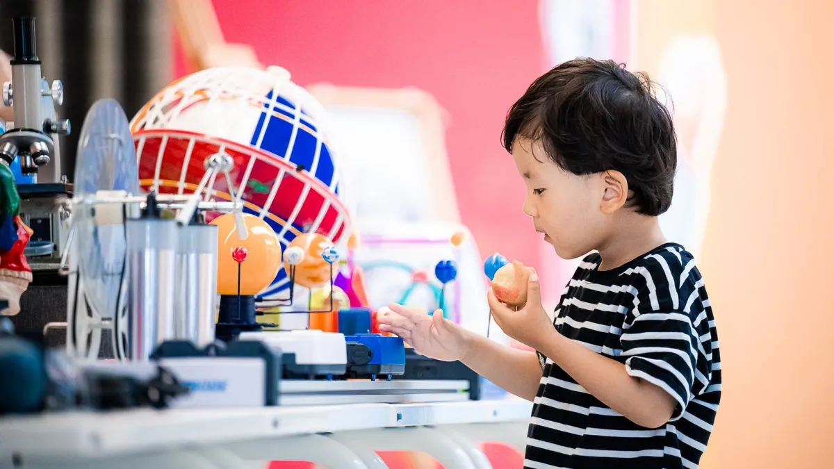 Ребёнок у стола с игрушками, в черно-белой полосатой футболке, с персиком в руках