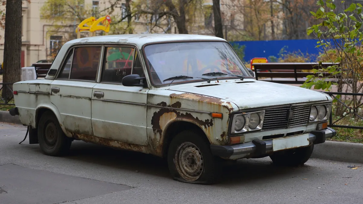 очень старый ржавый автомобиль машина жигули в дворе белая на фоне детской площадки