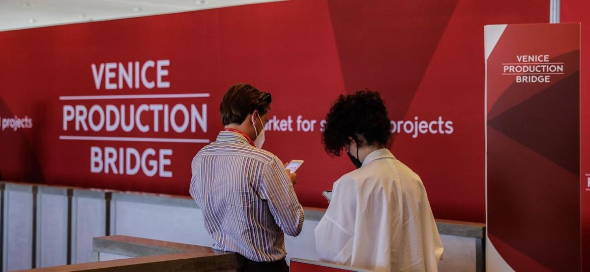 Venice Production Bridge двое мужчин в рубашках стоят спиной у стены, на красном фоне надпись Venice Production Bridge