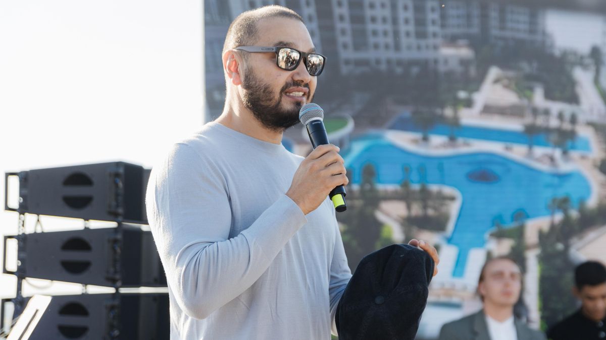 Еркин Татишев Еркин Татишев с микрофоном на фоне плаката с домом