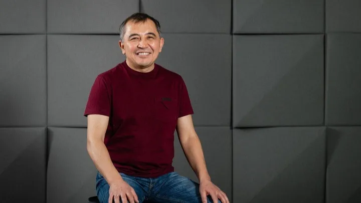 Серик Толукпаев Серик Толукпаев в бордовой футболке и джинсах сидит на стуле