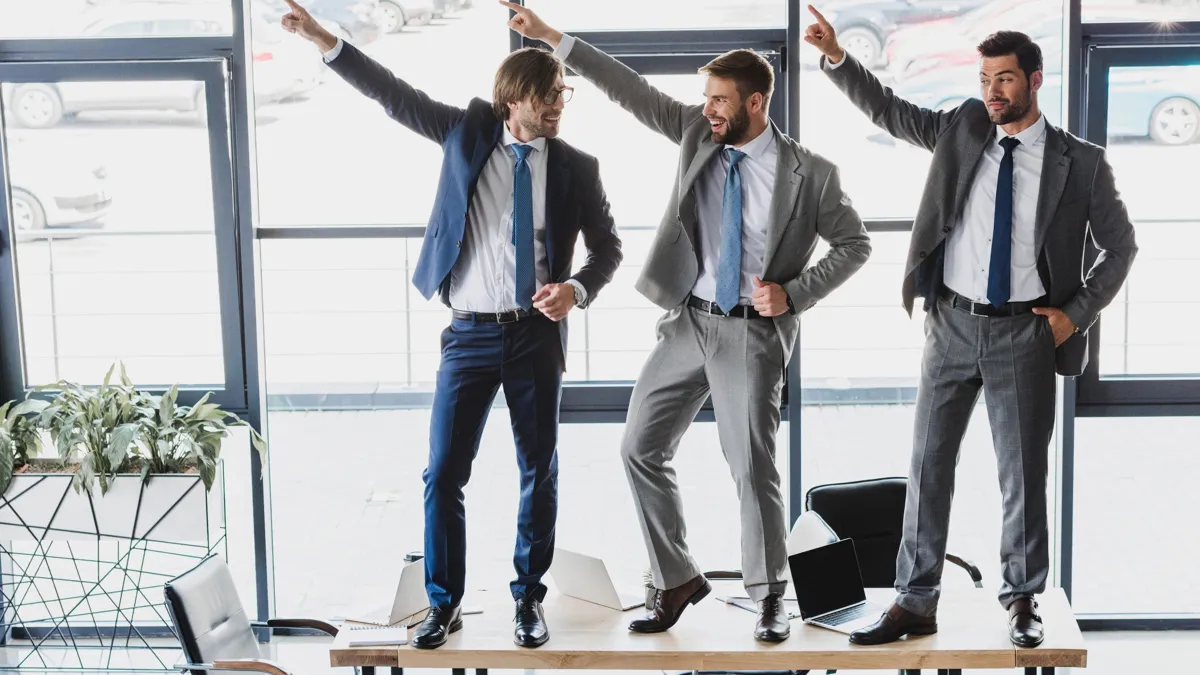 Many achievements in building good teams boil down to building a positive team culture that is the glue that holds a cohesive team together Три офисных работника танцуют на столе