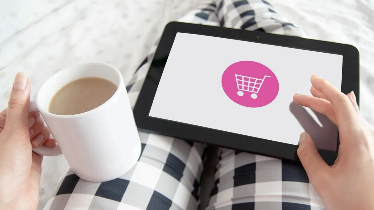 Маркетплейс, e-commerce, девушка в пижаме держит планшет с корзиной для покупок и чашку с чаем