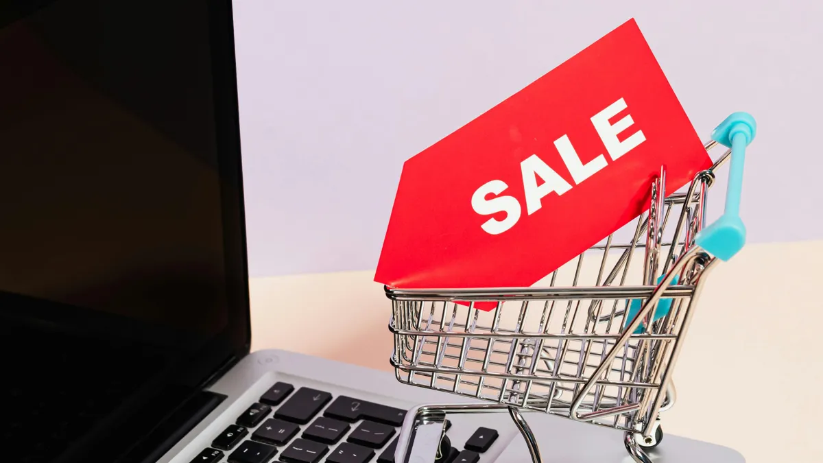 Миниатюрная тележка для покупок с табличкой Sale внутри стоит на открытом ноутбуке