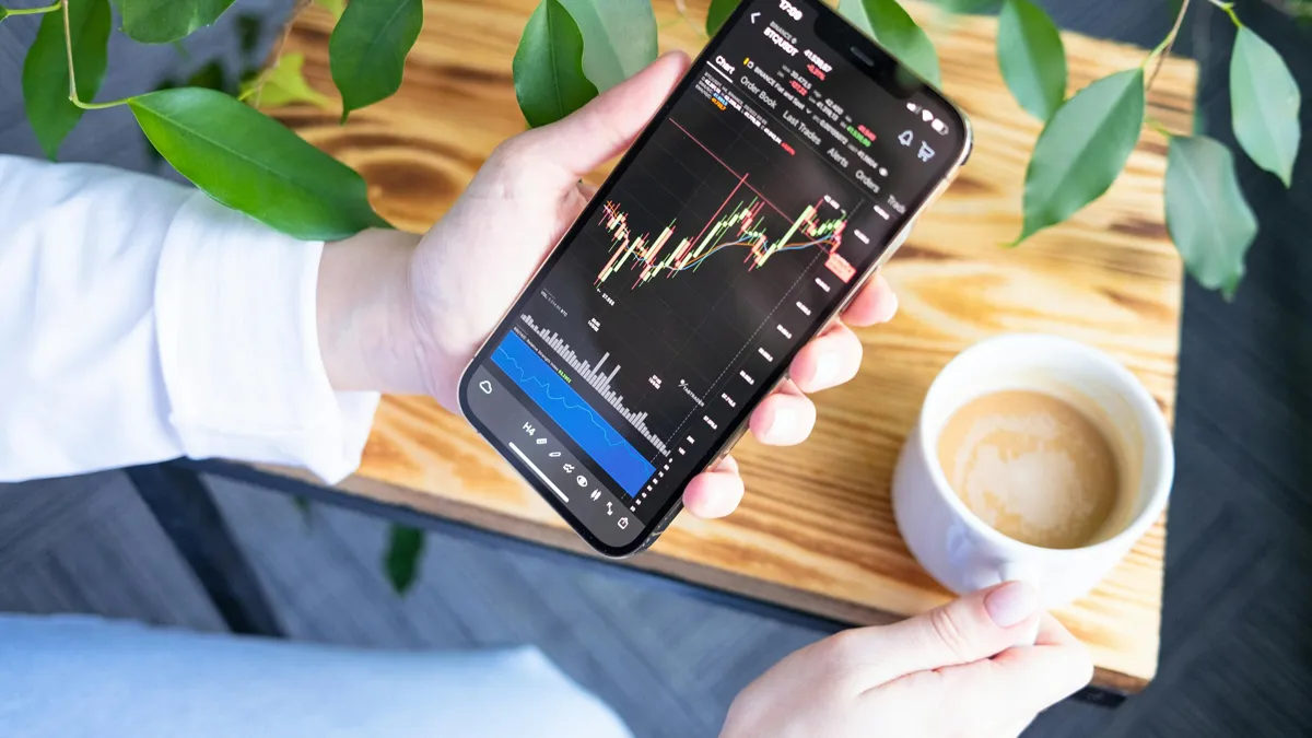 Девушка держит в руке смартфон с биржевыми графиками