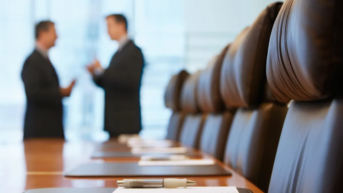 Два бизнесмена разговаривают в конференц-зале, справа — кожаные кресла