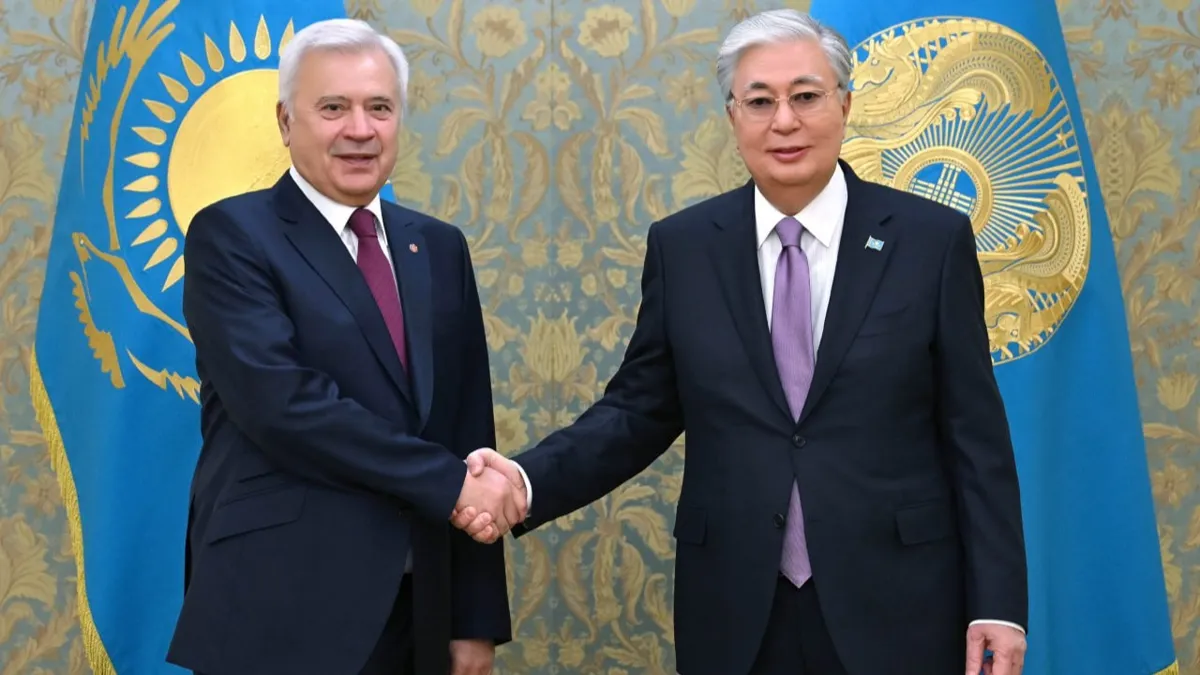 Вагит Алекперов и Касым-Жомарт Токаев пожимают руки друг другу на фоне флагов Казахстана и президента