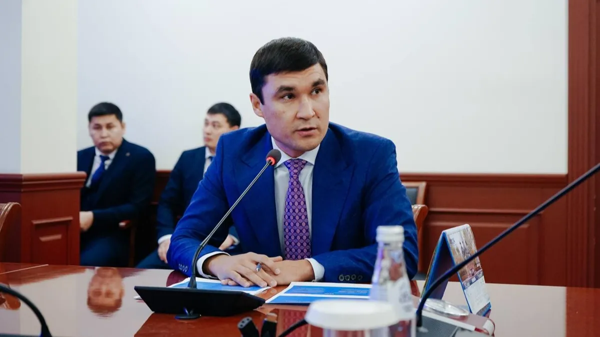 Серик Сапиев Серик Сапиев сидит за столом с синем костюме, перед микрофоном
