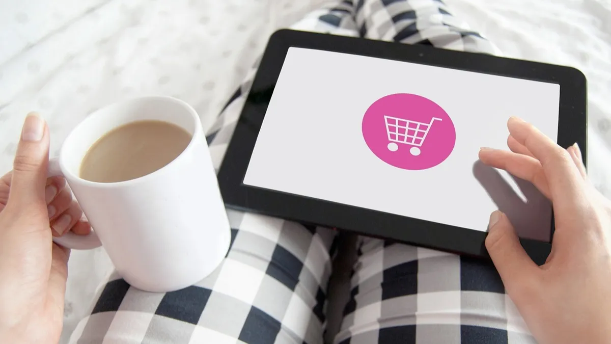Онлайн-торговля, e-commerce, девушка на планшете выбирает товары с чашкой кофе в руках