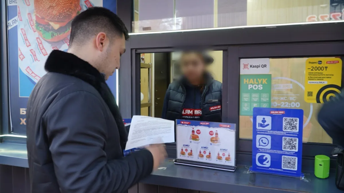 Полицейский протягивает документ в окошко торгового киоска в Алматы