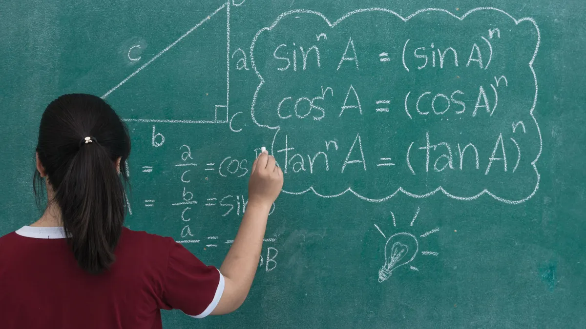 Школьница стоит у зеленой доски и пишет мелом математические формулы