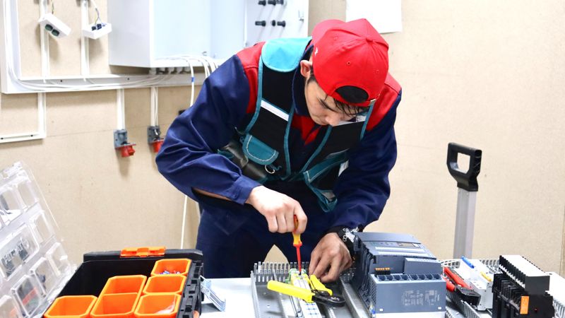 Молодой рабочий на производстве закручивает отверткой деталь
