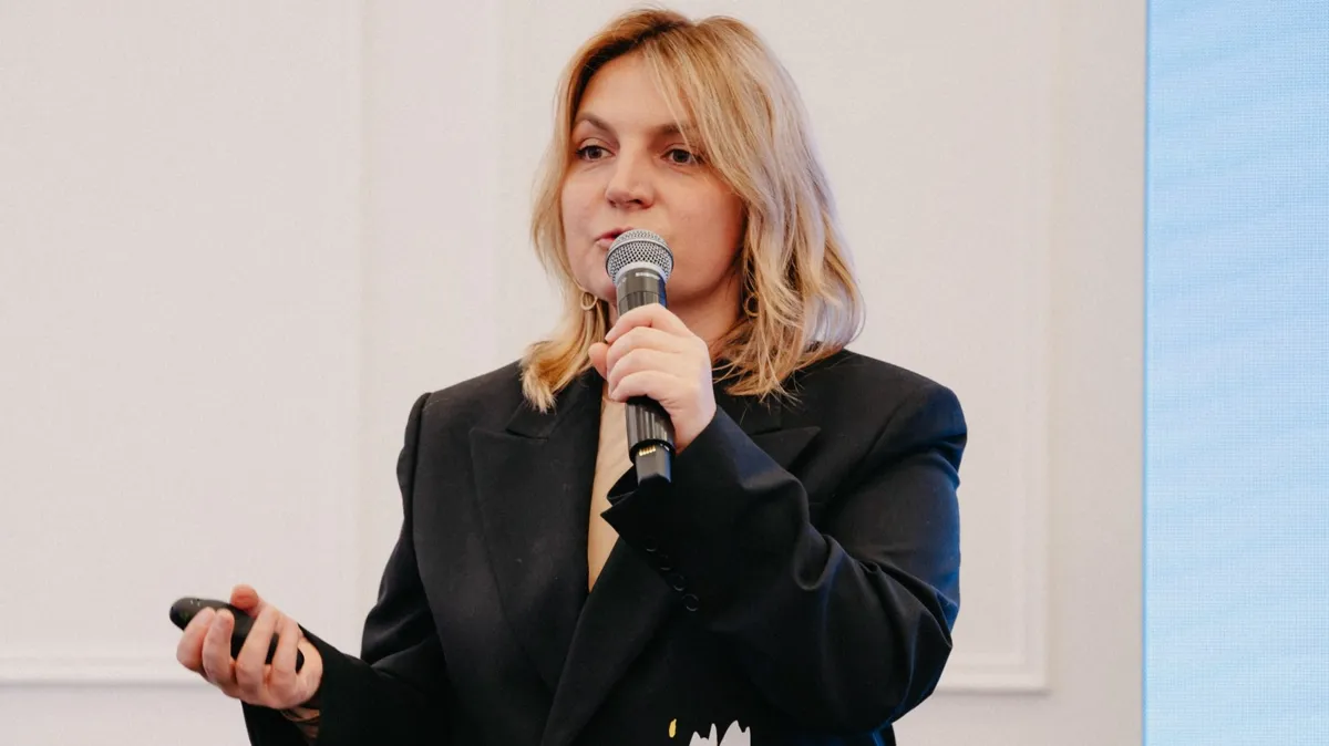 Анна Загоруйко с микрофоном и пультом в руках, апрель 2025, туристическая выставка