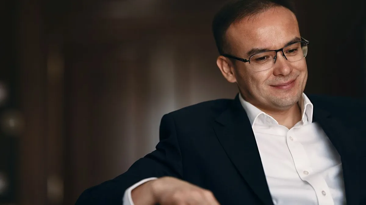 Бекжан Пирматов Бекжан Пирматов в белой рубашке и темном пиджаке, сидит, в очках