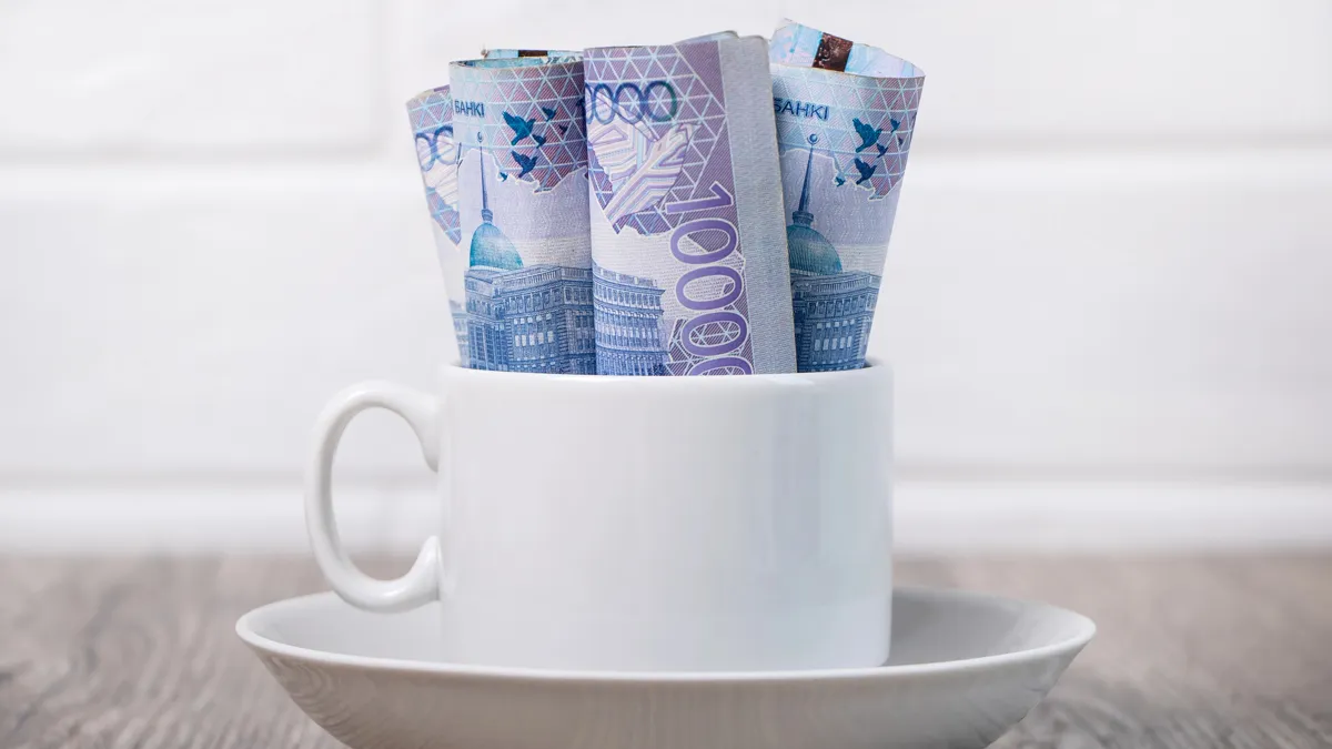 Купюры тенге, 10000, свернуты в кофейной чашке