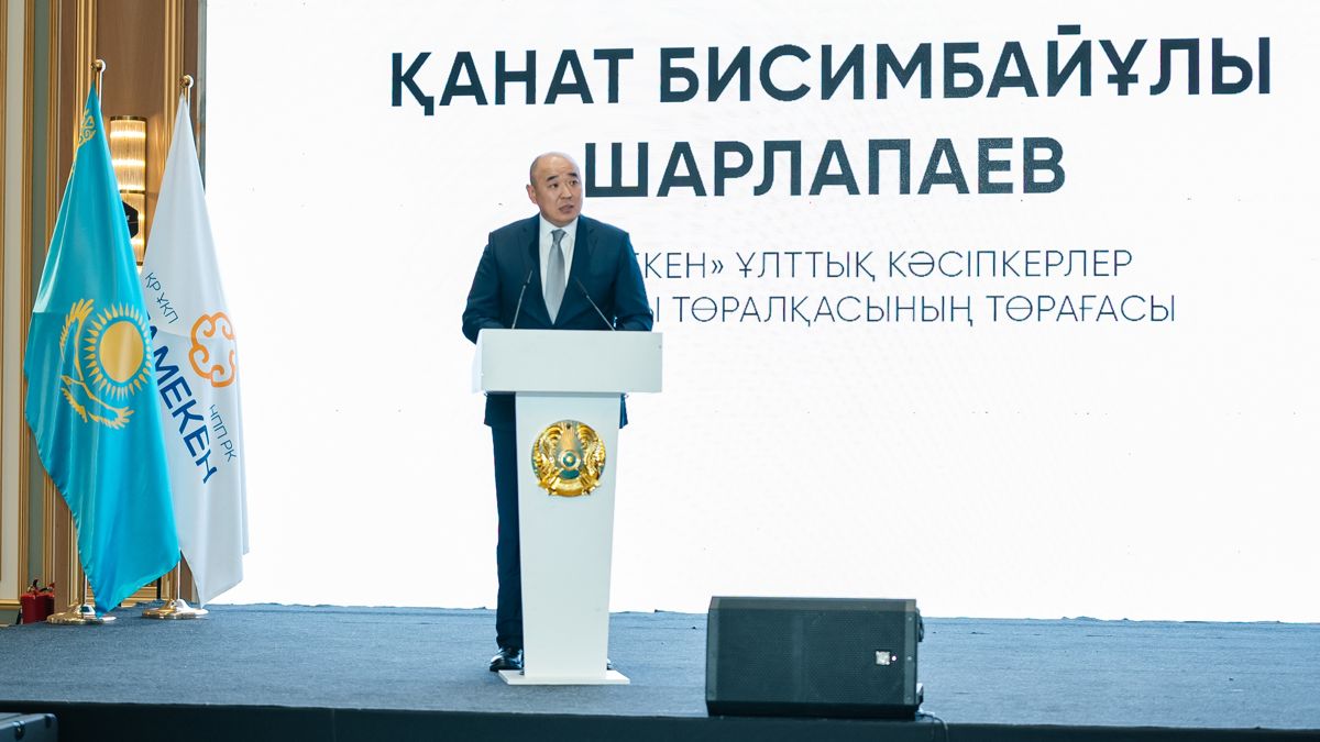 Канат Шарлапаев на фоне надписи - его имя на казахском